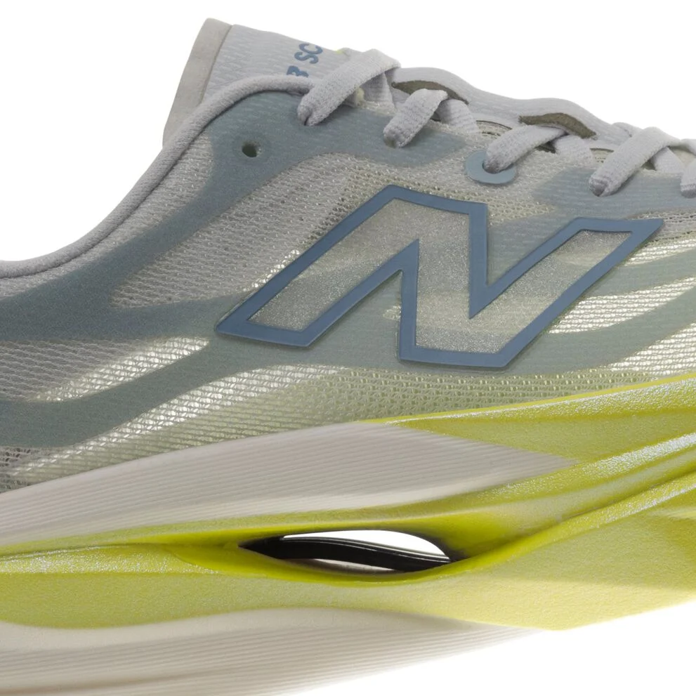 Close-up side view of a New Balance running shoe featuring a light gray mesh upper, blue &ldquo;N&rdquo; logo, white laces, and a lime-green sculpted midsole with a visible hollow cushioning design.